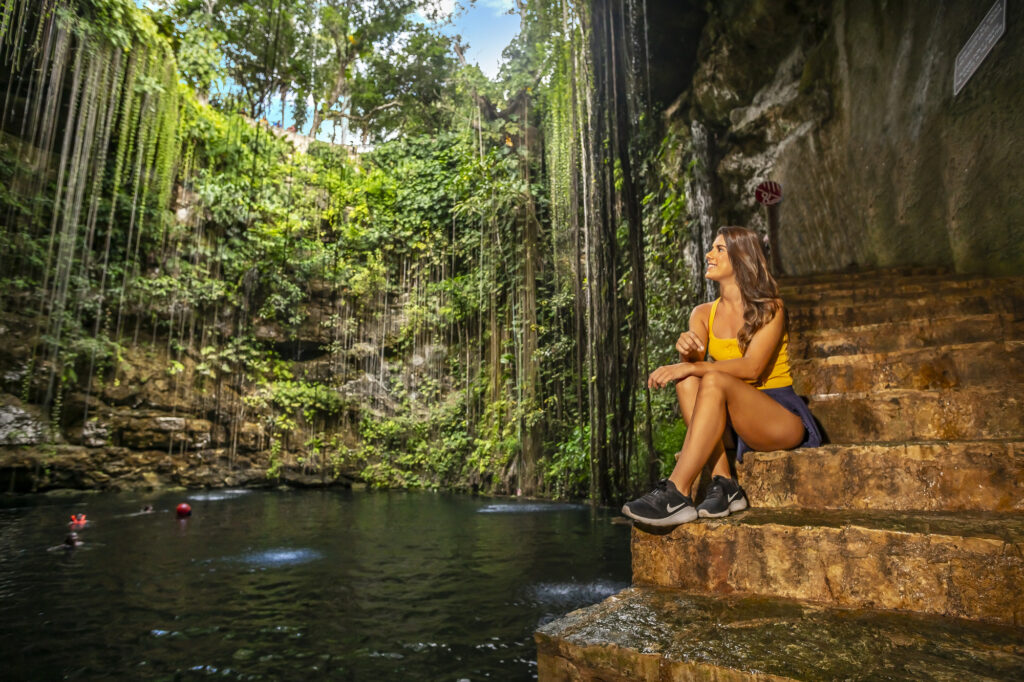 Young lady in yellow top resting next to a cenote during the Chichinitza Tour