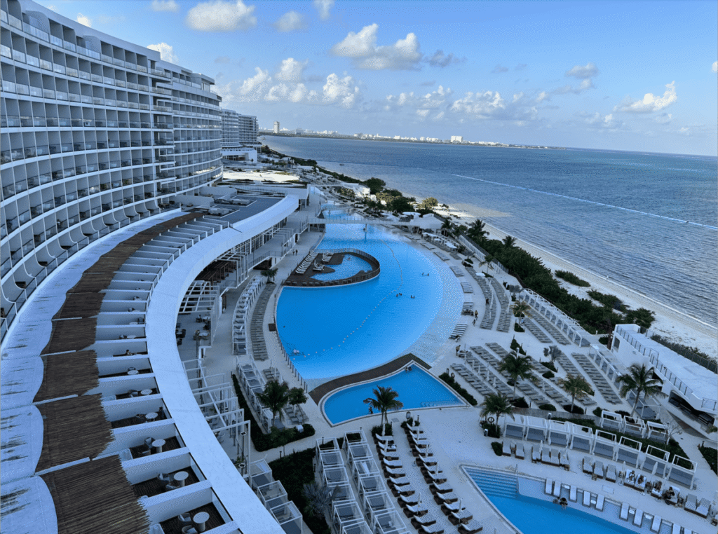 High-angle view of a large beachfront resort with multiple pools, lounge chairs, and panoramic ocean views - Ava Resort Cancun