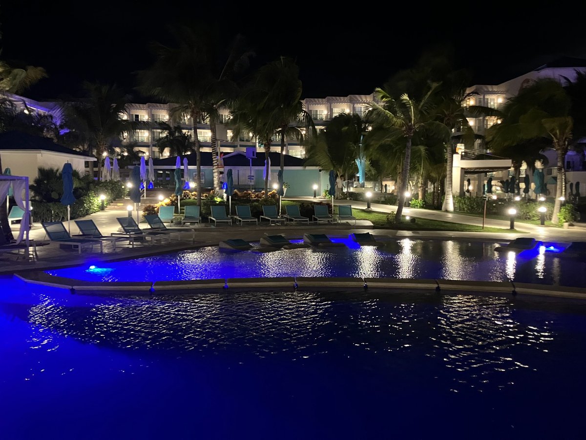 Pool area at night at Margaritaville Island Reserve Riviera Maya, with blue underwater lights and illuminated palm trees